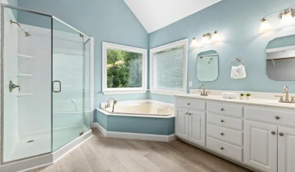 Bathroom with baby blue walls, tub, cabinets, and two mirrors