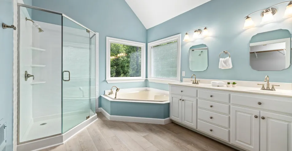 Bathroom with baby blue walls, tub, cabinets, and two mirrors